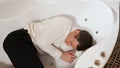 Man in trousers and a shirt is lying in the bath with a seizure