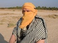 A man in a turban, face covered, with a camel in the Sahara desert