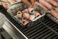 Man turning and roasting bacon wrapped dried plums, chicken filet and raw fresh sausages on gas grill BBQ barbecue in stainless