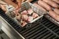 Man turning and roasting bacon wrapped dried plums, chicken filet and raw fresh sausages on gas grill BBQ barbecue in stainless Royalty Free Stock Photo