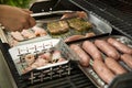 Man turning and roasting chicken filet, pork neck steaks, raw fresh sausages and bacon wrapped dried plums on gas grill BBQ Royalty Free Stock Photo