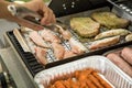 Man turning and roasting chicken filet, pork neck steaks, raw fresh sausages and marinated bacon wrapped skewers on gas grill BBQ