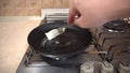A man turns on a gas burner, puts a pan on the stove and greases it with butter