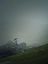 Man with umbrella climbing a mountain hill in a gloomy weather with dense mist. Moody hiking scene with a wanderer walking on the