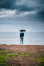 A man with an umbrella in the rain stands on a cliff and looks at the ocean back view. tourist place.