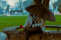 Man with umbrella sits under tree, holds red flower on park bench, rainy spring Royalty Free Stock Photo