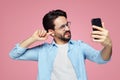 Man un-hygienically cleaning ear using finger with ticklish expression while using a smartphone