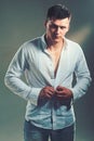 Man unbutton fashionable shirt. Young macho undress white shirt. Guy with serious face. Sexy model with elegant casual