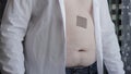 A man with an unbuttoned white shirt sticks a medical anti-smoking patch on his stomach, close-up. Tobacco addiction