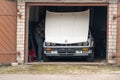 A man under the hood of white classic convertible BMW E30 car in the opened garage.