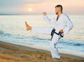 Man in uniform doing taekwondo exercises at sunset sea shore Royalty Free Stock Photo