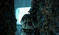 Man in uniform with machine gun and turned on night vision device between two brick walls. Airsoft soldier with green light on