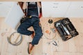 Man in uniform work in kitchen under sink. He repair water leaking. Hose and tools on floor. Opened toolbox. Royalty Free Stock Photo