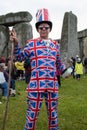 A man in a Union Jack Suit makes a peace sign at Stonehenge