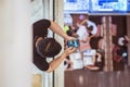 Man unsafely holds a smartphone outside the floor railing right above people who chill out below in a shopping mall