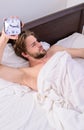 Man unshaven lay awake bed hold alarm clock. Stick sleep schedule same bedtime and wake up time. Man sleepy drowsy Royalty Free Stock Photo