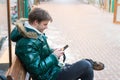 Man unshaven wear warm jacket and hold smartphone snowy urban background. Guy sit bench interact smartphone