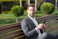 Man use smartphone in park. Manager with mobile phone on sunny outdoor. Businessman in blue suit sit on bench. Modern