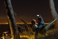 Man use smartphone Takes a selfie, photo picture. Couple relaxing in a hammock. View from the top of the mountain to the lights of