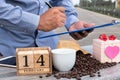 A man uses a laptop and drinks coffee in nature with a heart shaped gift box and wooden calendar. The concept of love on Royalty Free Stock Photo