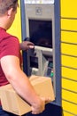 Man client using automated self-service post terminal machine or locker to depisit a parcel for storage