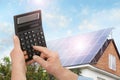 Man using calculator against house with solar panels. Renewable energy and money saving Royalty Free Stock Photo