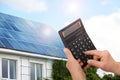 Man using calculator against house with solar panels. Renewable energy and money saving Royalty Free Stock Photo
