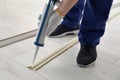 Man using caulking gun while installing plinth on laminated floor in room, closeup Royalty Free Stock Photo