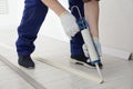 Man using caulking gun while installing plinth on floor in room, closeup Royalty Free Stock Photo