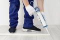 Man using caulking gun while installing plinth on laminated floor in room, closeup Royalty Free Stock Photo