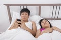 Man using cell phone while looking at woman sleeping in bed Royalty Free Stock Photo