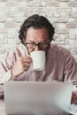 Man using computer at the desk in home office work place. Young mature caucasian people looking laptop display and drink coffee. Royalty Free Stock Photo