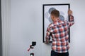 Man using cross line laser level for hanging painting on light wall, back view Royalty Free Stock Photo