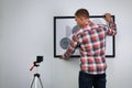 Man using cross line laser level for hanging painting on light wall, back view Royalty Free Stock Photo