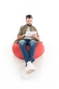 man using digital tablet while sitting on bean bag chair, Royalty Free Stock Photo