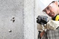 Man using an electric pneumatic drill making a hole in wall, professional construction worker with safety hard hat, hearing Royalty Free Stock Photo