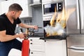 Man Using Fire Extinguisher To Put Out Fire From Oven