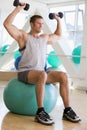 Man Using Hand Weights On Swiss Ball At Gym