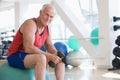 Man Using Hand Weights On Swiss Ball At Gym