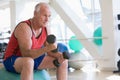 Man Using Hand Weights On Swiss Ball At Gym