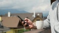 Man using his smartphone on the background of mountains and new houses.