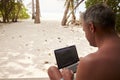 Man using a laptop computer on a beach, over shoulder view Royalty Free Stock Photo
