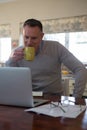 Man using laptop while having cup of coffee in living room Royalty Free Stock Photo