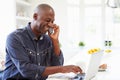 Man Using Laptop And Talking On Phone In Kitchen At Home Royalty Free Stock Photo