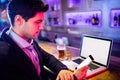 Man using mobile phone with glass of beer and laptop on table at bar counter Royalty Free Stock Photo