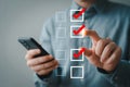 Man using mobile phone for online checklist app with red checkmarks and boxes on digital interface Royalty Free Stock Photo