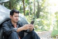 Man using phone for contact maintenance car service. Traveler sitting and using smartphone while Broken car