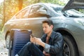 Man using phone for contact maintenance car service. Traveler sitting and using smartphone while Broken car with luggage