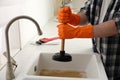 Man using plunger to unclog sink drain in kitchen