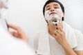 Man using razor to shaving his face with cream foam in bathroom mirror Royalty Free Stock Photo